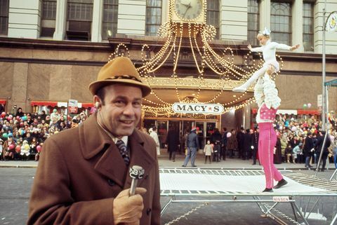 joe garagiola, 1970 yılında macy'nin şükran günü geçit töreninde arka planda akrobatlarla mikrofona konuşuyor