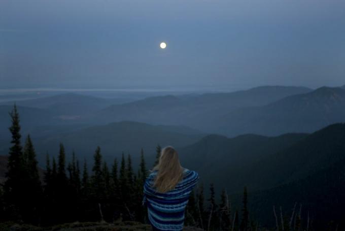 battaniyeye sarılı kadın dolunay ve arka görüşle dağlık araziye bakıyor