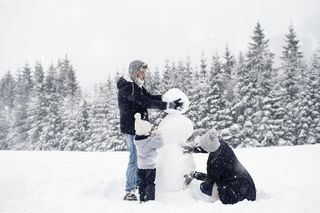 karda bir kardan adam inşa eden üç kişilik aile