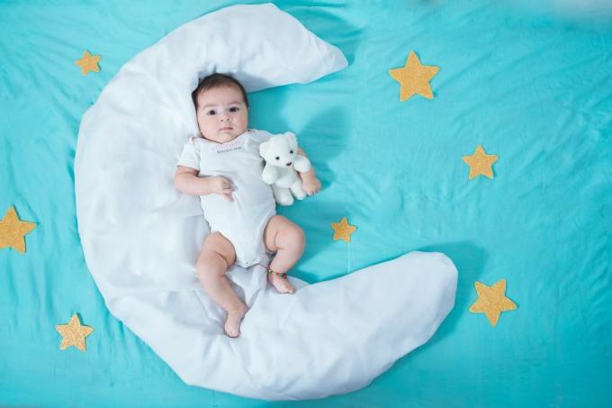 güzel latin kız bebek, iki aylık, her iki yanında sarı yıldızlar ve altında mavi bir çarşaf olan ay şeklinde beyaz bir çarşafın üzerinde yatıyor