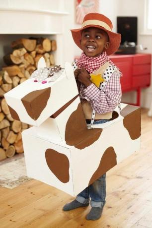 kovboy şapkalı, ekose gömlekli ve belinin etrafında karton atlı bandanalı kovboy gibi giyinmiş küçük çocuk