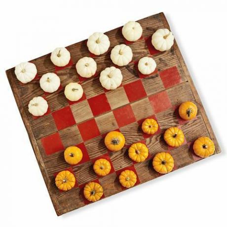 Oyun parçaları olarak beyaz ve turuncu mini balkabakları kullanan bir dama oyunu gibi boyanmış ahşap bir tahta