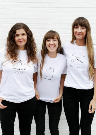 beyaz tişörtlü üç kadın, gömleğin üzerine taş, kağıt veya makas yazılı ve resimli