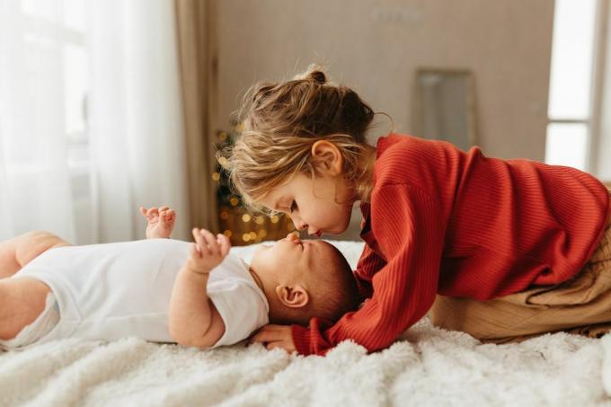 sevimli çocuk beyaz yatak üzerinde yatan küçük kız kardeşini öpüyor