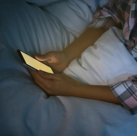 Geceleri yatakta akıllı telefon kullanan kadın, yakın çekim nomofobisi ve uyku bozukluğu sorunu
