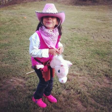 Küçük bir kız, bir hobi atı olan bir kovboy kız gibi pembe giyinmiş.