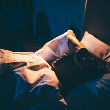 Uykusuzluk çeken genç kadın yatakta uzanmış, eli alnında