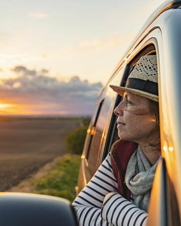 40'lı yaşlarındaki bir kadın karavanından kırsal bölgenin manzarasını izliyor, halinden memnun ve rahat görünüyor