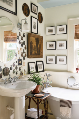 Duvarında vintage sanat eserleri ve pençe ayaklı küvet bulunan toplu banyo