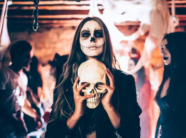 Cadılar Bayramı partisinde kafatası tutan iskelet makyajlı genç kadın
